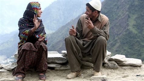 A man and a woman engaged in a lively conversation while seated on a rocky ledge, set against a mountainous backdrop.